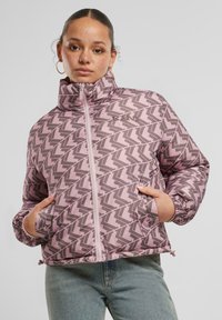 Rožinis pūkinis švarkas su geometriniu pilku raštu, aukštu apykakle, dviem priekinėmis kišenėmis, elastingais rankogaliais ir su raišteliu apatine dalimi, pagamintas iš blizgaus medžiagos.
