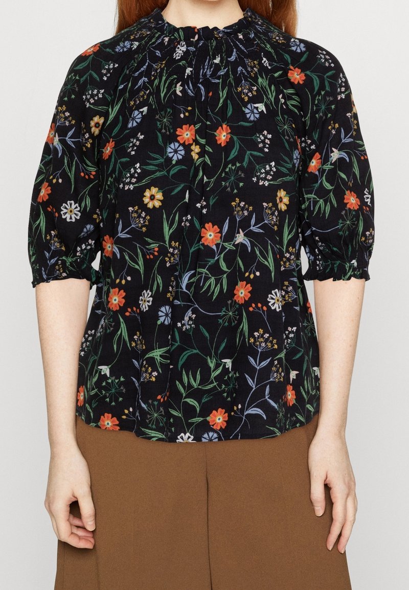 Blommig blus med svart bakgrund, prydd med livfulla flerfärgade blommor, puffärmar och rynkad halsdetalj. Hållbar tygtextur.