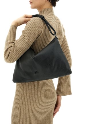 Donna che indossa un abito beige a coste e porta una grande borsa a tracolla di pelle nera con texture, con una cinghia larga appoggiata sulla spalla.