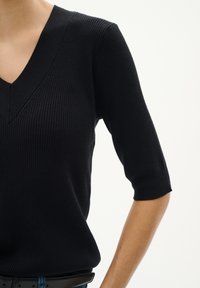 Černý žebrovaný úpletový top s výstřihem do V a krátkými rukávy. Tkanina má hladkou strukturu a přiléhavý střih, doplněný černým páskem.