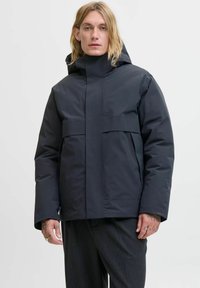 Donkere, gewatteerde jas met een hoge kraag en capuchon. Voorzien van voorzakken, een gladde textuur en een minimalistisch ontwerp. Zwarte kleur.