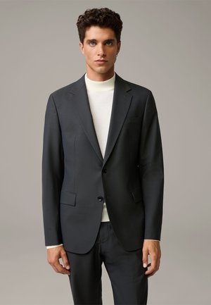 Men's dark gray tailored suit jacket with a subtle pattern, two buttons, notch lapels, and angled pockets. Paired with a light turtleneck.