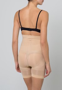 Beige shaping shorts with a high-waisted design, smooth texture, and elastic waistband. Visible seams and a mid-thigh length.