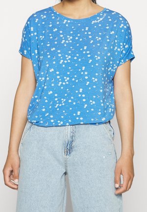 Woman wearing a blue t-shirt with small white daisy flowers paired with light blue high-waisted jeans.