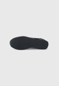 Black shoe sole with a textured surface. Features horizontal grooves for traction. Material appears rubber with a rounded toe design.