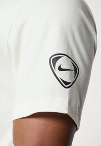 Hvid bomulds t-shirt med et sort Nike-logo på ærmet. Stoffet har en glat tekstur og et klassisk design med korte ærmer.
