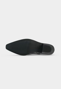 Semelle de chaussure habillée en cuir noir avec bout pointu et petit talon empilé, vue du dessous sur un fond uni.