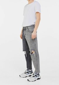 Gray and black distressed jeans with ripped detailing, paired with a white T-shirt and black and white athletic sneakers.