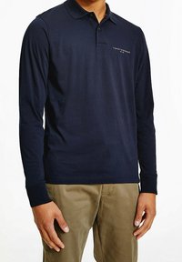 Marineblaues Langarm-Polohemd aus Baumwolle, klassischer Kragen, gesticktes Logo auf der Brust, kombiniert mit hellen Khaki-Hosen.