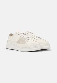 Weiße Sneakers mit beigen Akzenten, die ein niedriges Profil, ein Schnürdesign und eine dicke Sohle aufweisen, vor einem schlichten Hintergrund.