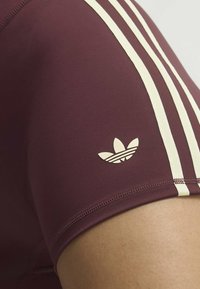 Close-up of a maroon sport sleeve with three white stripes and a white Adidas trefoil logo near the hem.