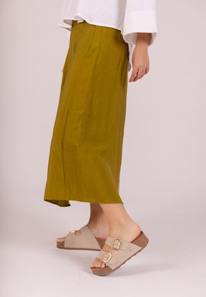 Jupe mi-longue vert olive en tissu léger avec une texture subtile. Sandales à glissière beige avec deux boucles en ton or et des semelles texturées.