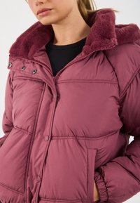 Pufferjack in mauve met een zachte, gestructureerde kraag. Voorzien van drukknopen en gestikte delen. Inclusief zijzakken voor gemak.