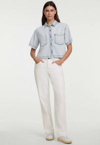 Lyseblå denimskjorte med korte ærmer, knaplukning foran, to brystlommer og cropped design, kombineret med hvide bukser med vide ben.