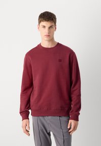 Sudadera burdeos de mezcla de algodón, con cuello redondo, puños y dobladillo acanalados, que presenta un pequeño parche de logo texturizado en el pecho.