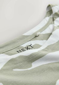 Gros plan sur un col en tissu rayé vert et blanc avec des coutures visibles et une étiquette de marque "NEXT" imprimée à l'intérieur.