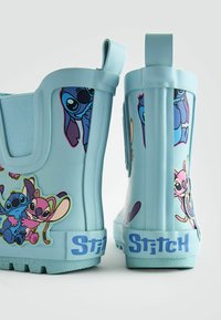 Blå gummistövlar med grafiska mönster av Stitch och Angel. Stövlarna har en slät yta och en texturerad sula med ett dragband.