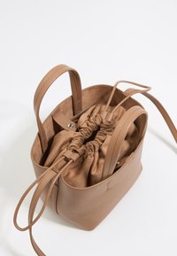 Brązowa skórzana torba typu bucket z zaciąganym zamknięciem, gładką powierzchnią i dwoma krótkimi uchwytami, wykończona miękką podszewką z materiału.