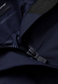 Interior de chaqueta azul marino con un zipper negro, textura de tela suave y etiqueta que indica la talla "Mediana."