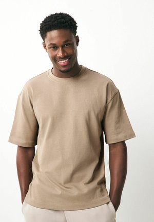 Beige t-shirt met korte mouwen, ronde hals en een ontspannen pasvorm; gemaakt van katoen, met een gladde textuur en minimale stikseldetails.