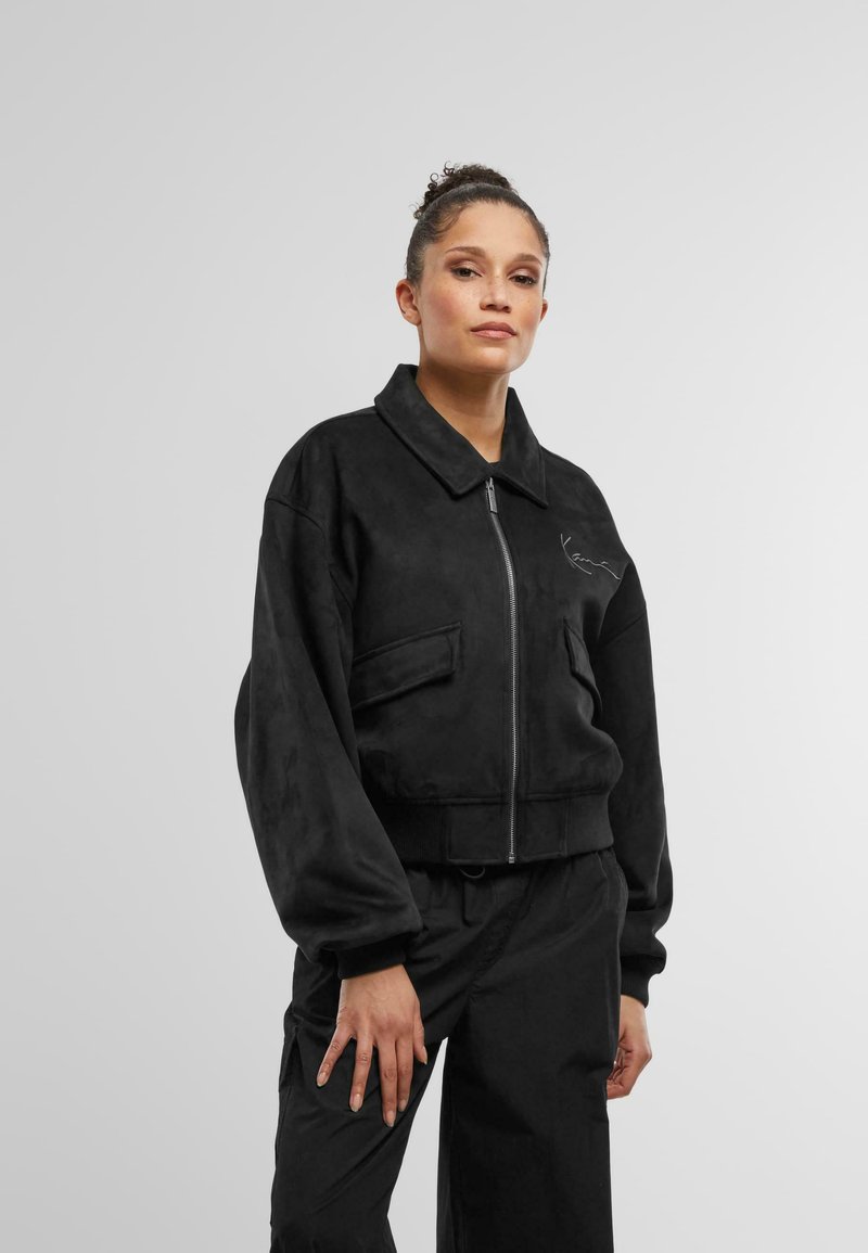 Jachetă neagră scurtă dintr-un material moale asemănător cu suede, cu guler, fermoar frontal și buzunare laterale. Accentuata cu o cusătură minimalistă.