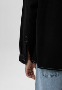 Zwarte spijkerbroeken met witte stiksels, zijslitsen en een losse pasvorm, gecombineerd met lichtblauwe spijkerbroek.