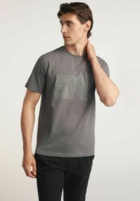 Szara bawełniana koszulka z geometrycznym nadrukiem linii z przodu. Krótkie rękawy i okrągły dekolt, w zestawieniu z ciemnymi spodniami.