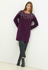 Maglione viola a maniche lunghe con un motivo di leopardo decorativo in strass sul collo, abbinato a pantaloni neri a sigaretta e stivali alla caviglia.
