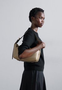 Sac à main en cuir beige avec une texture lisse et une forme arrondie, doté d'une courte bandoulière et de peu d'accents en métal.