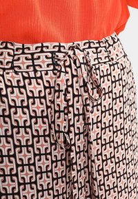 Spódnica w wzory z różowo-białym geometrycznym wzorem i czarnymi akcentami. Posiada związany pas i miękką, teksturowaną tkaninę.