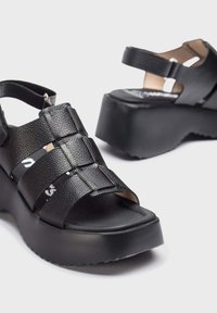 Sandalias de plataforma negras hechas de material texturizado con tres correas anchas y hardware en tono dorado, que cuentan con una plantilla contorneada y una suela resistente.