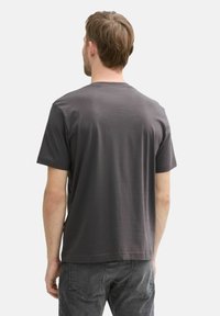 Gray cotton t-shirt with short sleeves, round neck, and a smooth texture, viewed from the back. Worn with dark jeans.
