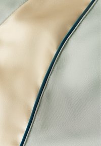 Tessuto con sezioni crema e verde chiaro dalla texture liscia, separate da un sottile bordo color verde teal scuro.