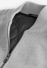 Gray bomber jacket made of soft fabric with a ribbed collar and black lining, featuring a metal zipper and minimal stitching details.