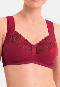 Soutien-gorge bordeaux avec un détail en dentelle sur le dessus, des bretelles larges et un accent en nœud. Fabriqué en tissu lisse, il présente une conception de soutien-gorge avec armatures.
