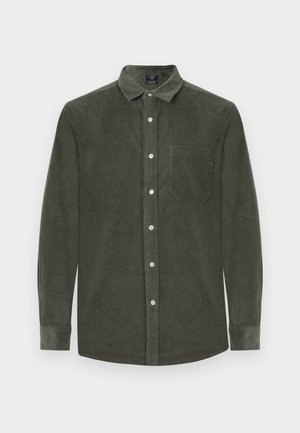 Ελαιοπράσινο πουκάμισο από καπιτονέ ύφασμα με μακριά μανίκια, κλείσιμο με κουμπιά και τσέπη στο στήθος. Διαθέτει κλασικό γιακά και υφασμάτινη υφή.