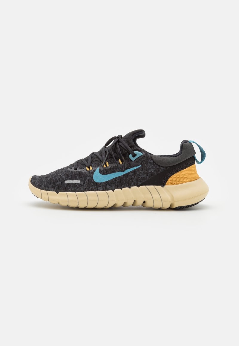 Baskets de sport noires avec semelle marron clair, logo Nike bleu, languette de talon bleue et détail de talon jaune moutarde, vues de côté.