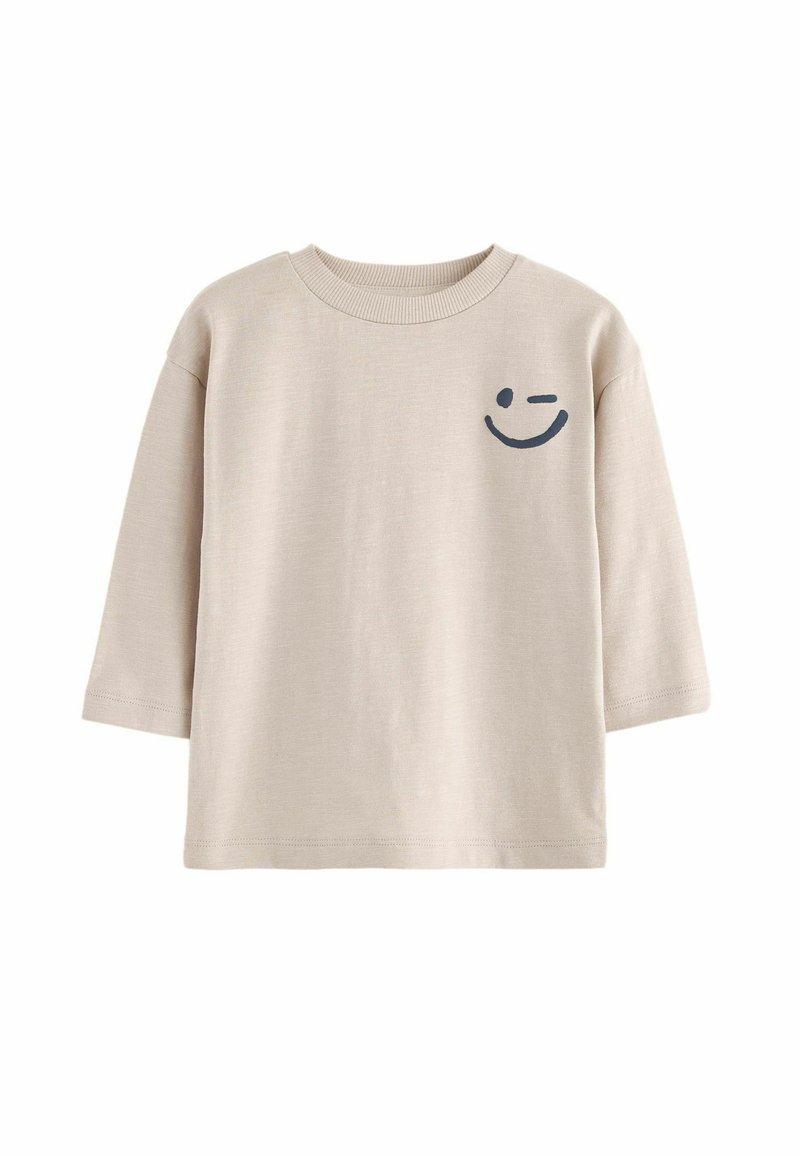 T-shirt en coton beige à manches trois quarts, col rond, avec un graphique de smiley bleu foncé sur la poitrine gauche.