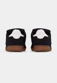 Ζεύγος μαύρα αθλητικά παπούτσια χαμηλού ύψους με καφέ σόλες, που φαίνονται από πίσω, με λευκά τακούνια με ανάγλυφα λογότυπα.