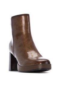 Botín de tobillo de charol marrón con punta redonda, tacón alto y ancho, y un acabado texturizado sutil. La suela gruesa acentúa el diseño moderno.