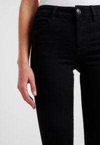 Sorte denimbukser med slim fit, fem lommer og metallknappelukking. Glatt tekstur med minimal sømdetalj.