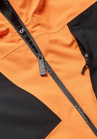 Waterdichte jacket met oranje stof en zwarte accenten, een getextureerde rits en gelabelde zwarte ritsband.