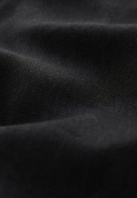 Tessuto nero con una trama liscia e strutturata. Leggero lucido e lievi variazioni di colore creano profondità. Nessun motivo o accento visibile.