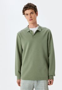 Grün langärmliges Poloshirt aus weichem Stoff, mit einem kragenförmigen Ausschnitt, drei Knöpfen und einer lockeren Passform.