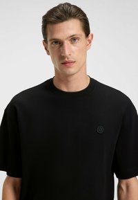Zwarte katoenen t-shirt met een ronde halslijn, korte mouwen en een subtiele geborduurde logo op de linkerborst. Glad textuur.