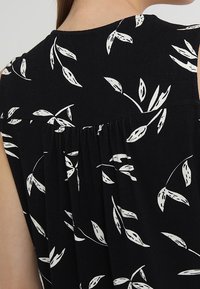 Top negro sin mangas con un estampado floral blanco de hojas, con un detalle de espalda fruncido para añadir textura. Tejido ligero.
