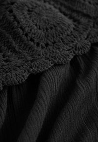 Sort stof med et struktureret hæklede mønster og fine ribber. Materialet er blødt med draperede, flydende elementer.