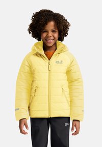 Chaqueta acolchada amarilla con capucha, con cierre de cremallera y bolsillos laterales. El material es suave y acolchado, con detalles reflectantes.