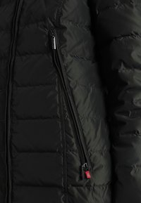 Svart puffjacka med quiltat mönster, som har en ficka med dragkedja på sidan, slät textur och en subtilt blank yta.