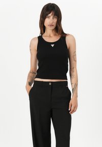 Svart ribbet crop tank topp med rund halslinje og sølvfarget trekant accent; paret med høyt liv svarte bukser.